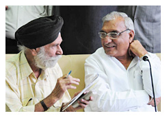 मुख्यमंत्री हुड्डा के बिलकुल बगल में बैठकर उन्हें समझाते पत्रकार एसएन परवाना
