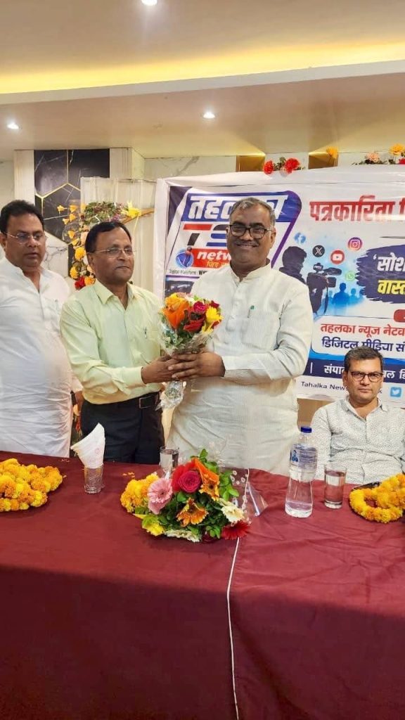 1c165ece-58b7-4546-83af-f06ea37a775a | No. 1 Indian Media News Portal Two men exchange a bouquet at a formal event, with a banner and flower arrangements on the table in front of them.