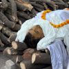 Deceased person wrapped in white shroud lying on stacked firewood, with a marigold garland around the neck."