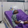 Adult patient lying on a hospital bed with an IV drip connected and purple bedding in a clinical room