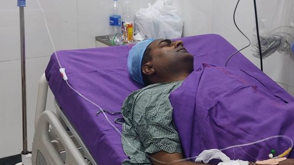 Adult patient lying on a hospital bed with an IV drip connected and purple bedding in a clinical room