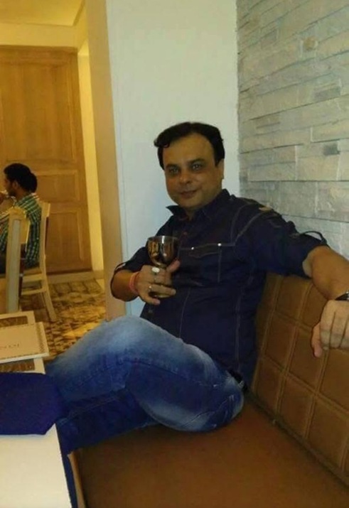 Man sitting on a tan sofa in a restaurant, holding a wine glass and looking at the camera.