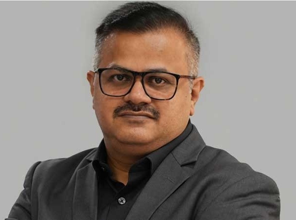 Professional head-and-shoulders portrait of a man wearing black shirt and dark suit with glasses, looking at the camera.