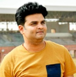 Young man wearing an orange shirt with a dark pocket, standing outdoors and looking to the left.