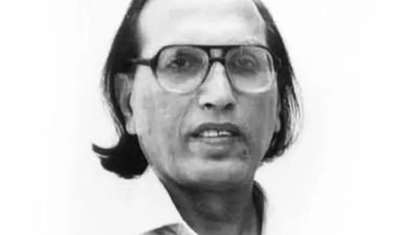 Black-and-white head-and-shoulders portrait of a man with glasses and medium-length hair, looking at the camera.