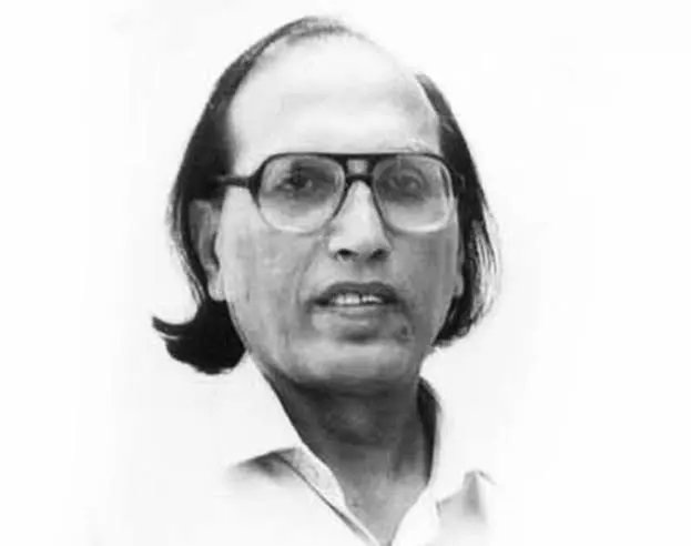 Black-and-white head-and-shoulders portrait of a man with glasses and medium-length hair, looking at the camera.