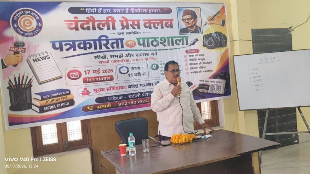 chandauli press_1 | No. 1 Indian Media News Portal Speaker standing at a table with a microphone during a journalism workshop, colorful Hindi banner in the background praising press ethics and reading skills.