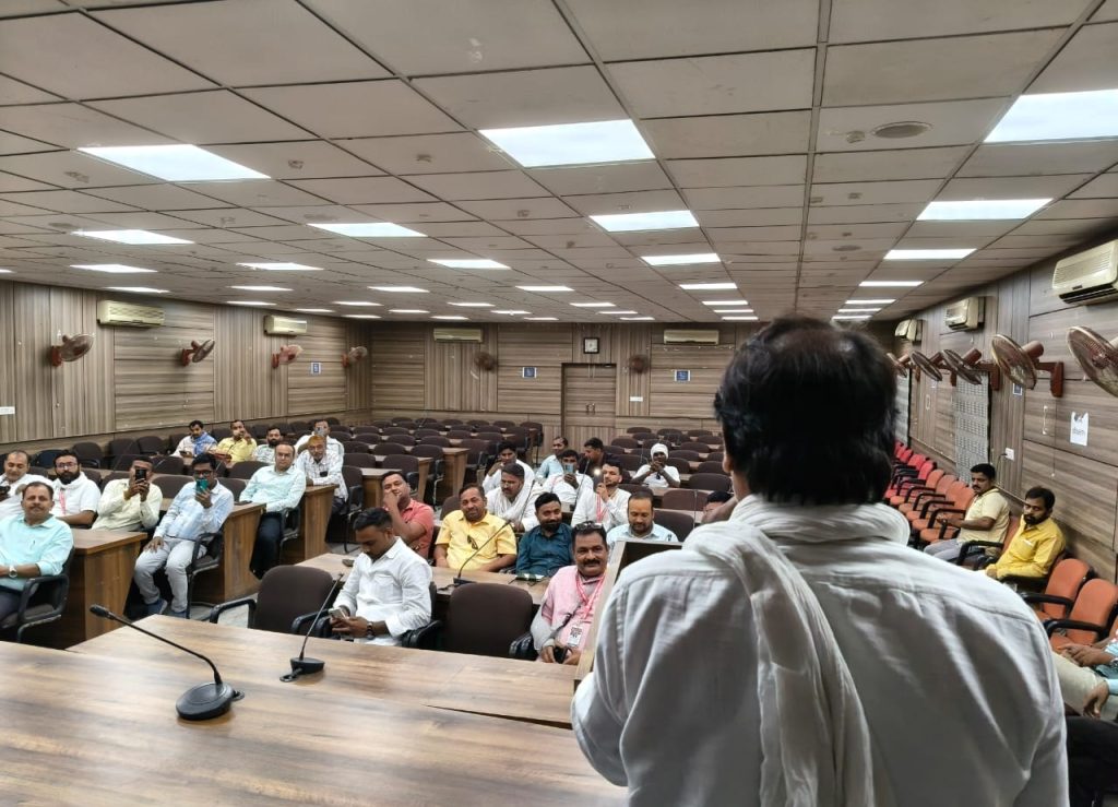 ghazipur samman | No. 1 Indian Media News Portal Speaker at a wooden lectern addressing a seated audience in a wood-paneled lecture hall viewed from behind the speaker's shoulder edge.
