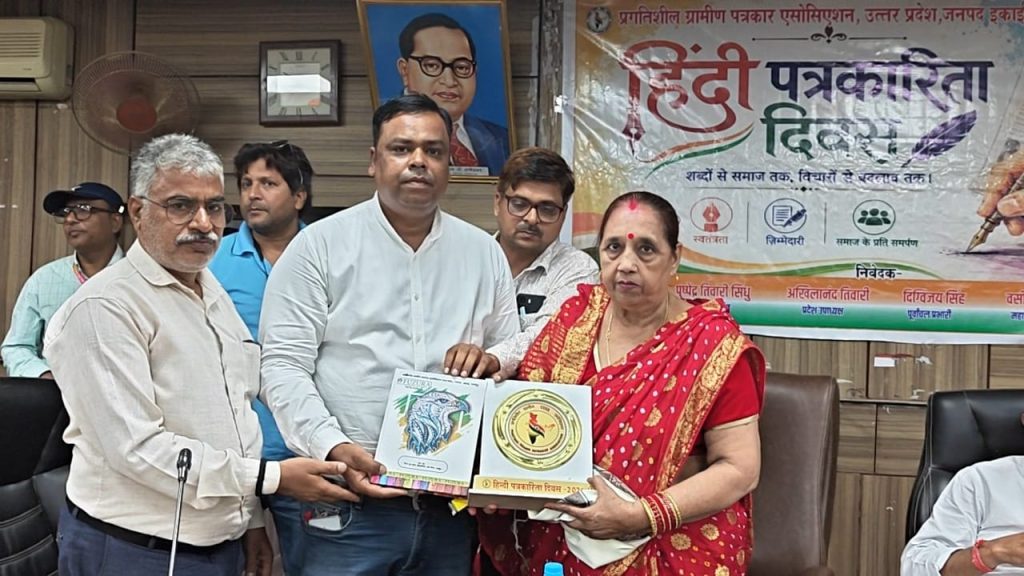 ghazipur samman_2 | No. 1 Indian Media News Portal Group of men and a woman in a red saree stand in a conference room, presenting and receiving two awards/plaques with a banner in Hindi about a journalism event behind them.
