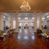 Elegant hotel lobby with a grand chandelier, white columns, and a symmetrical seating area of striped sofas and glass tables with yellow flowers.