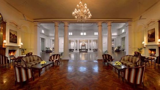 Elegant hotel lobby with a grand chandelier, white columns, and a symmetrical seating area of striped sofas and glass tables with yellow flowers.