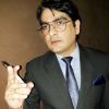 Man in a dark suit and glasses holding a marker and pointing toward the camera, as if presenting.
