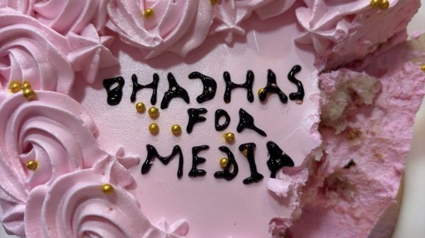 Pink frosted cake with many rose-like swirls and gold beads, a single pink candle, and a bite taken from the side; message partially visible on the cake surface.