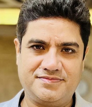 Close-up portrait of a man with dark hair and a slight smile, wearing a light shirt.