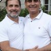 Two men in white polo shirts smiling at the camera while shaking hands outdoors.