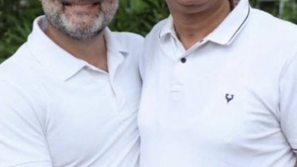 Two men in white polo shirts smiling at the camera while shaking hands outdoors.