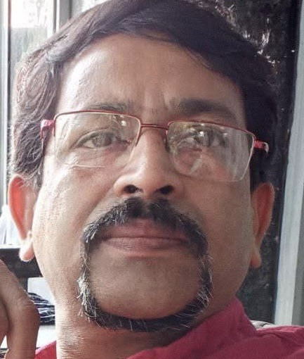 Close-up portrait of a man with a mustache and goatee wearing glasses and a red shirt, looking at the camera.
