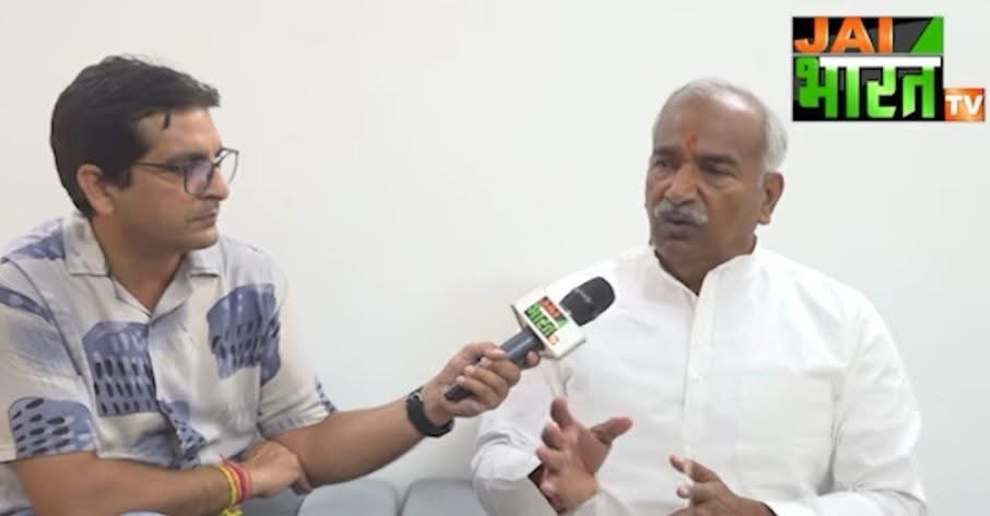 News interview scene: journalist with glasses interviews a man in a white kurta; microphone labeled with JAI BHARAT TV logo in the corner.