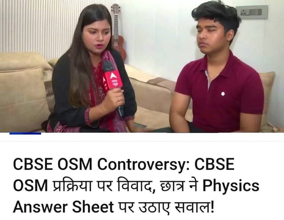 Female reporter with a red microphone interviewing a man seated on a beige sofa in a living room; a bold news headline about CBSE OSM controversy is visible below.