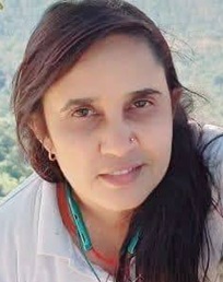 Close-up portrait of a woman with dark hair outdoors, wearing a white shirt.