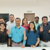 Eleven coworkers posing in an office, many flashing peace signs and smiling at the camera.