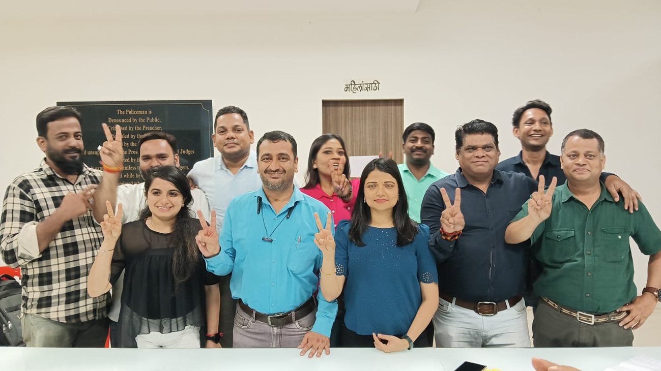 Eleven coworkers posing in an office, many flashing peace signs and smiling at the camera.
