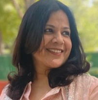 Smiling woman outdoors with trees in the background, wearing a pink top.