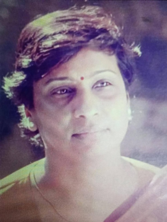 Portrait of an Indian woman with short dark hair, wearing a small red bindi and light makeup, looking slightly to the left with a gentle smile