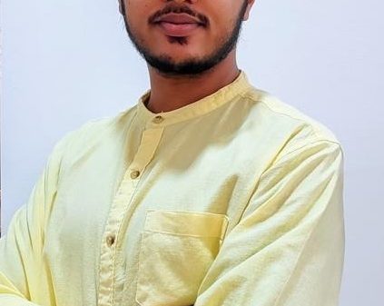 Man with short dark hair and glasses wearing a pale yellow kurta, arms crossed, looking at the camera.