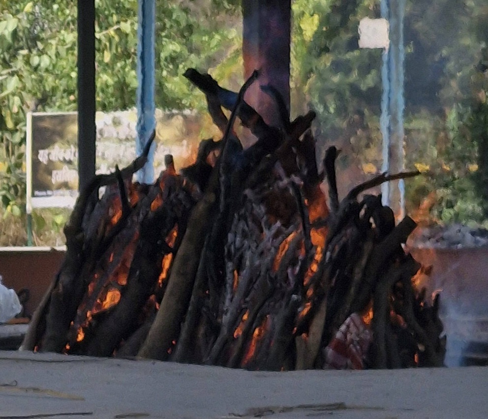 raj_ | No. 1 Indian Media News Portal Large bonfire with burning stacked logs under a pavilion, orange flames licking the wood.