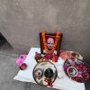 Framed portrait on a small roadside altar with orange marigold garlands, surrounded by fruit, flowers, and ritual bowls on a white cloth.