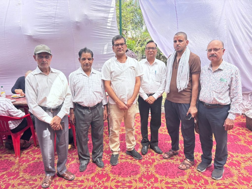 Six men stand side by side for a group photo at an outdoor event under a light tent, dressed in smart casual clothes.