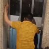 Man in a yellow shirt seen from behind, pressing against or attempting to open the elevator doors inside a building lobby.