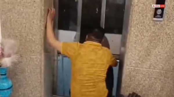 Man in a yellow shirt seen from behind, pressing against or attempting to open the elevator doors inside a building lobby.