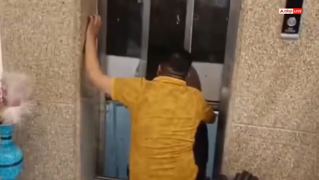 Man in a yellow shirt seen from behind, pressing against or attempting to open the elevator doors inside a building lobby.