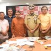 Group of colleagues and a police officer posing in a newsroom office with a red backdrop behind them.