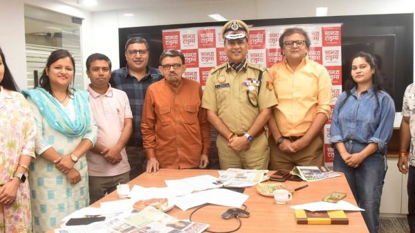 Group of colleagues and a police officer posing in a newsroom office with a red backdrop behind them.