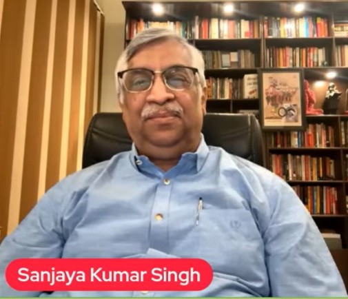 Sanjaya8 | No. 1 Indian Media News Portal Man with glasses wearing a light blue shirt sits in a chair in front of a bookshelf-filled background; a red caption badge is visible at the bottom.
