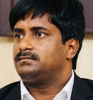 Portrait of a man with short black hair and a mustache, wearing a white shirt and dark blazer, looking to the left.