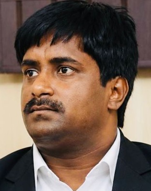 Portrait of a man with short black hair and a mustache, wearing a white shirt and dark blazer, looking to the left.