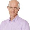 Smiling bald man with glasses wearing a lavender button-down shirt, facing slightly to the right.