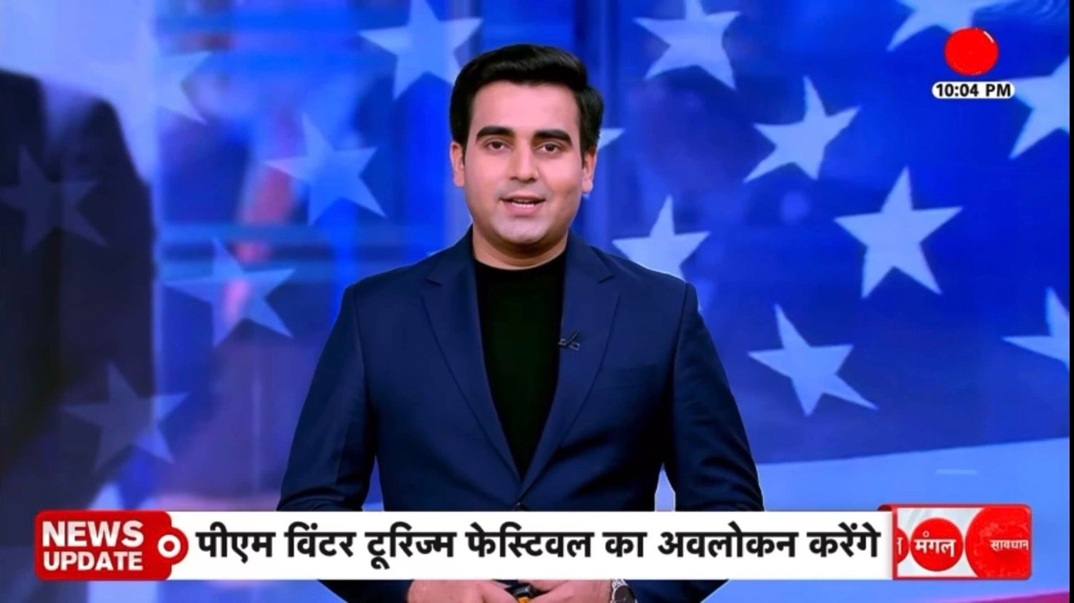 News anchor delivering a broadcast in a blue studio with star backdrop and a red 'News Update' banner at the bottom (Hindi ticker).