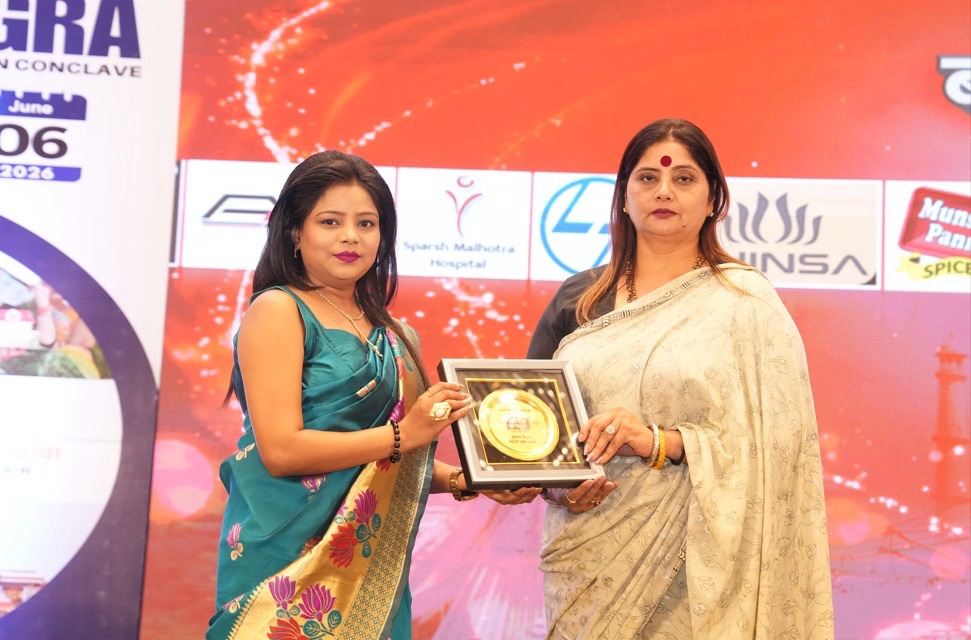 a9cf5fc9-4f13-4d2f-9d65-e7606aa28350 | No. 1 Indian Media News Portal Two women on stage exchange a framed award against a red backdrop with sponsor logos.