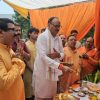 Men perform a Hindu ritual with offerings on a table under orange drapes at a ceremonial gathering.