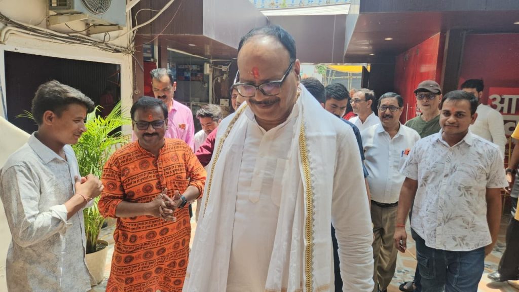 aaj ki khabar_2 | No. 1 Indian Media News Portal Man in white traditional attire with tilak and a gold-trimmed shawl walks among a group of men at an outdoor gathering.