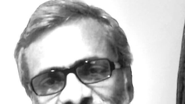 Grayscale portrait of a bearded man with glasses; Hindi headline above.