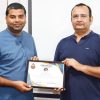 Two men stand and hold a framed certificate of appreciation between them, posing for the camera.