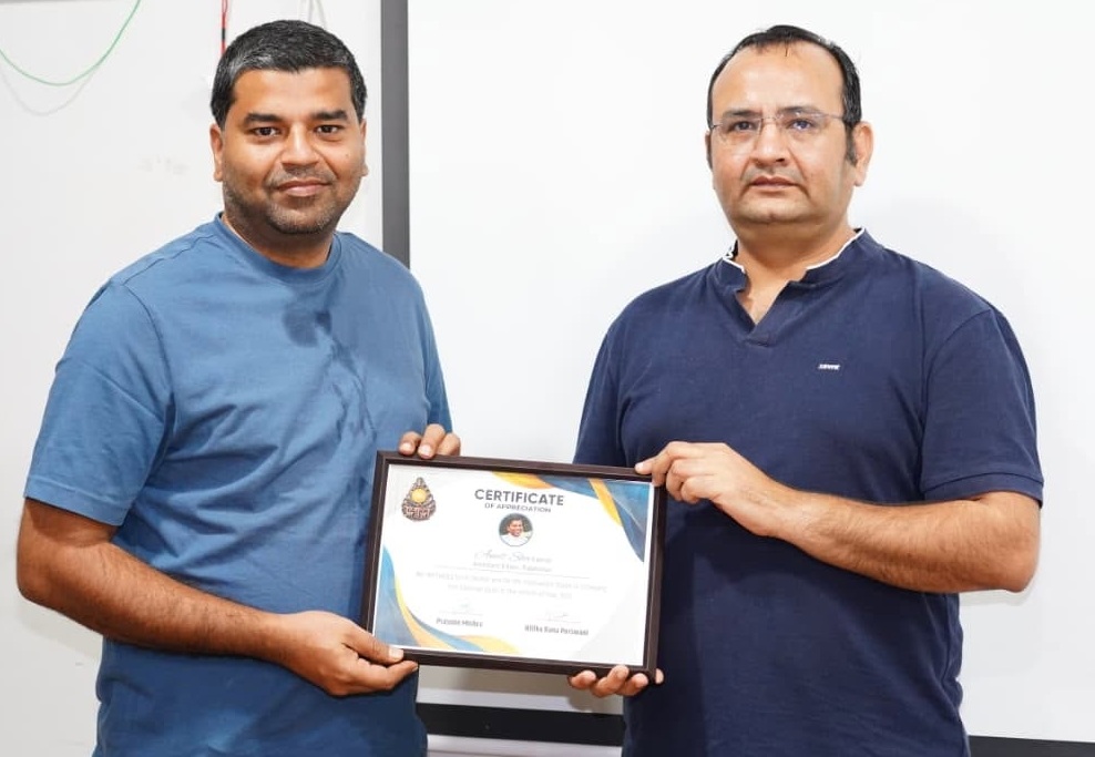Two men stand and hold a framed certificate of appreciation between them, posing for the camera.