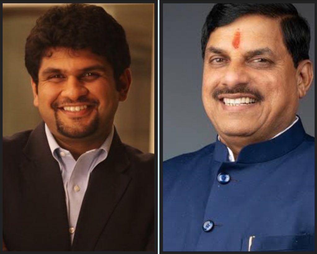 Two men smiling for the camera, standing side by side; left man in a dark suit, right man in a blue Nehru-style jacket.