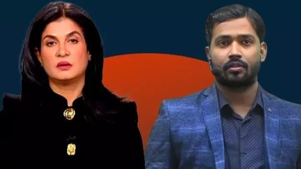 Two news hosts standing side by side against a dark blue backdrop with an orange semicircle behind them, the woman in black with gold buttons and the man in a blue blazer.